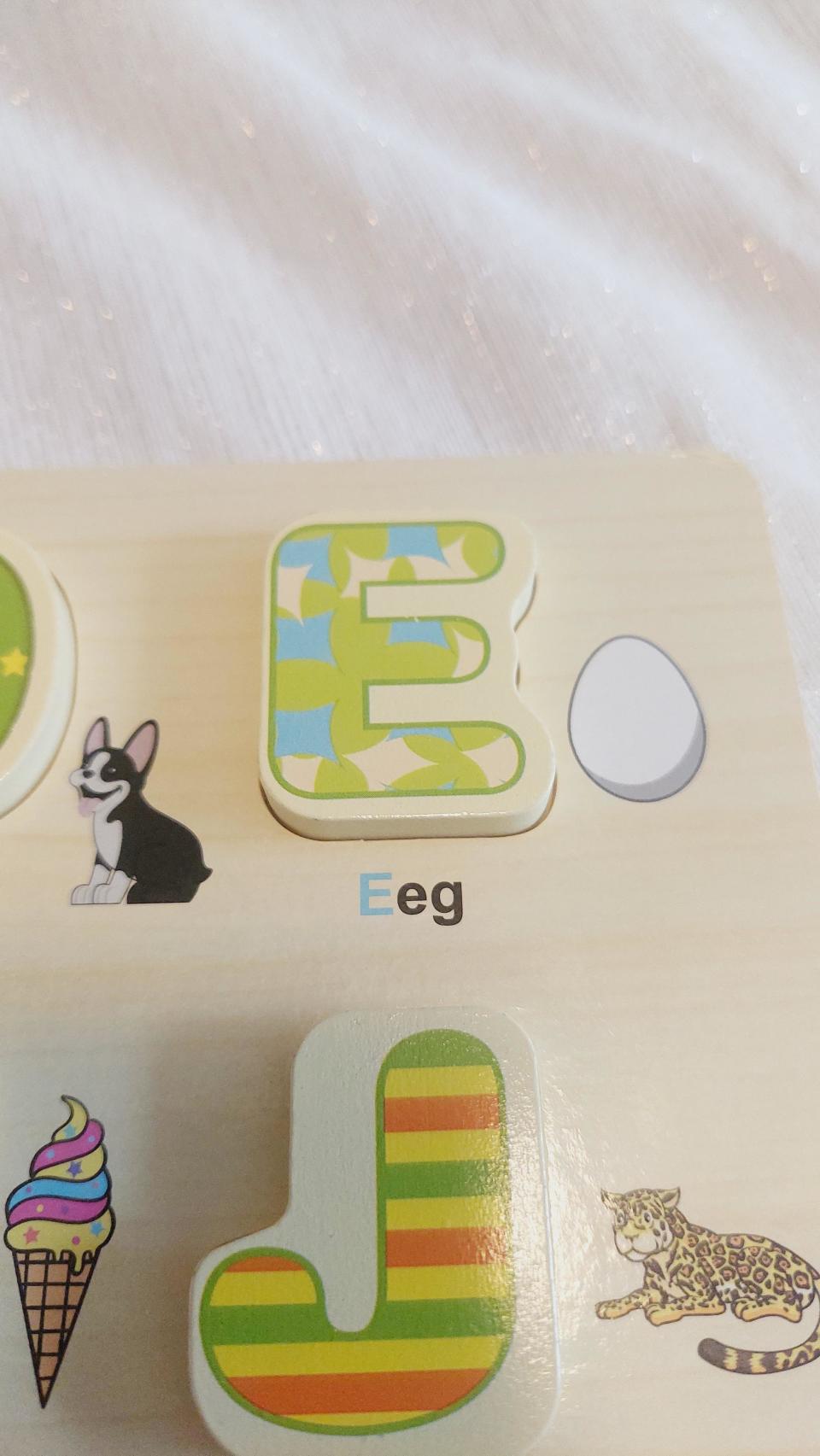 A wooden puzzle showing the letter 'E' with a green pattern, a cartoon dog, an egg, ice cream, a colorful 'J', and a leopard illustration