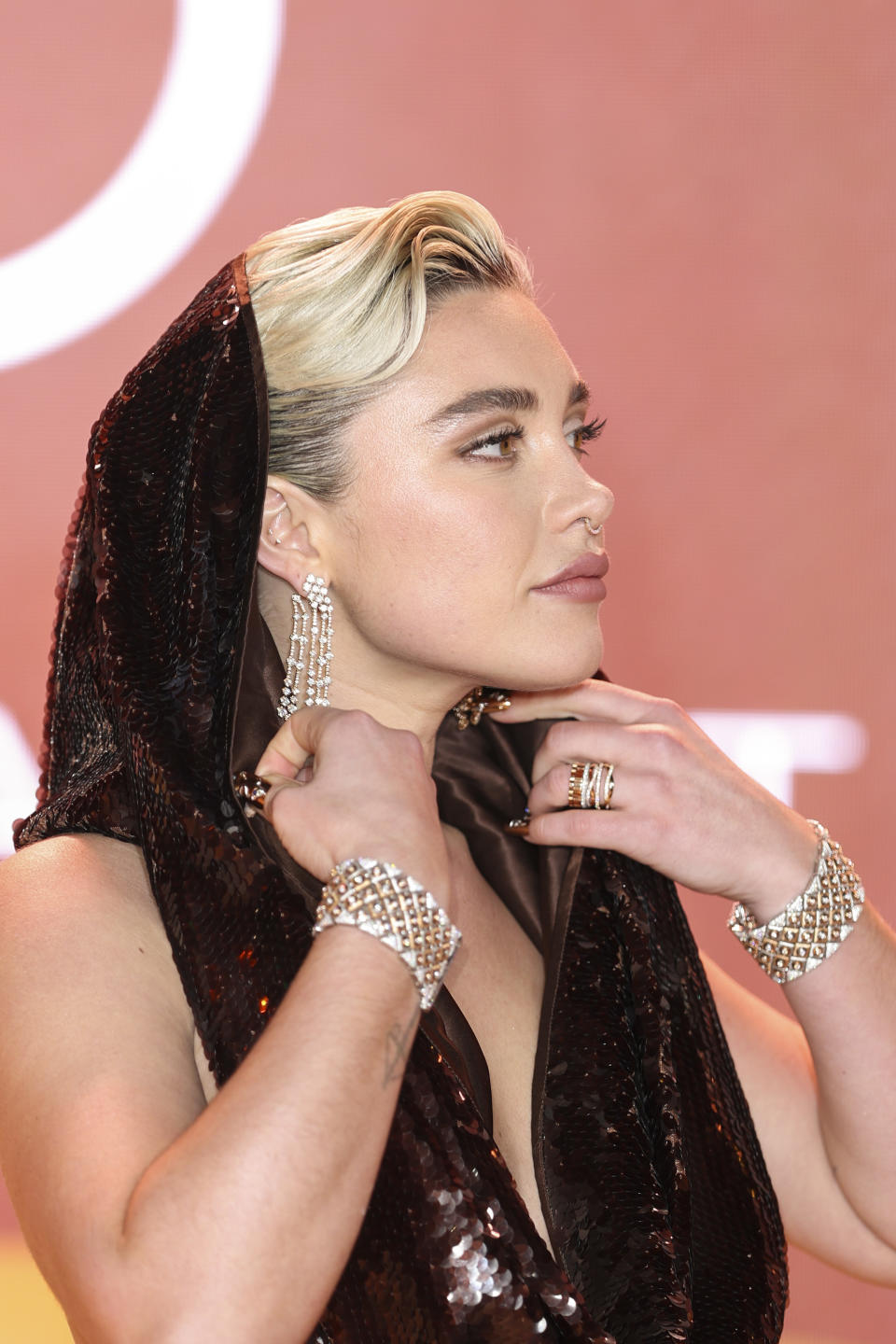 Florence Pugh wears a sparkly outfit with a hood with bracelet cuffs and long earrings