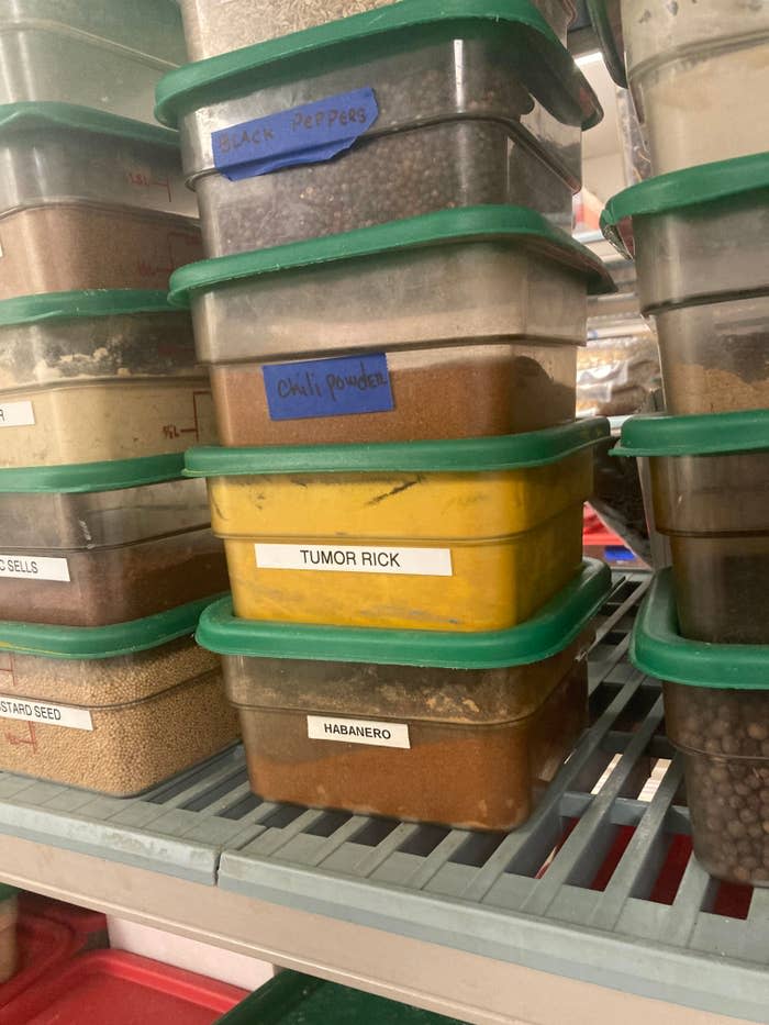 Stack of labeled spice containers, including chili powder, turmeric, and habanero, on a kitchen shelf