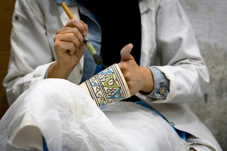 Hands painting a piece of pottery with a ceramic pattern