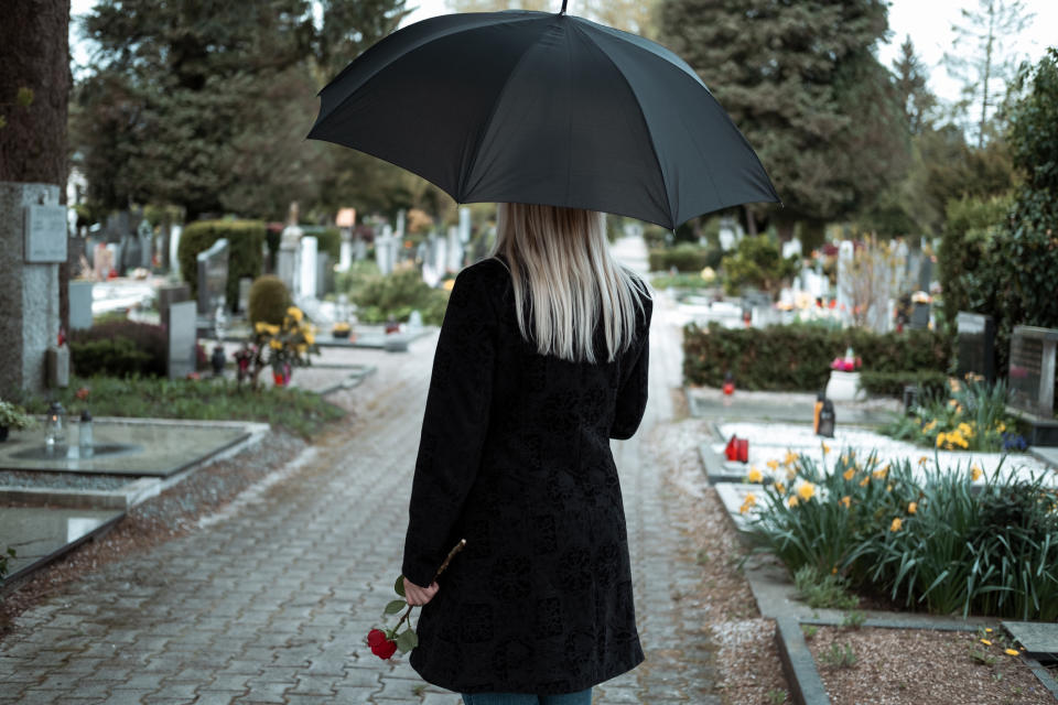 Person with umbrella and rose in a cemetery, viewed from behind