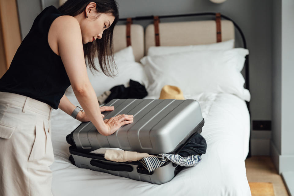 Person packing a suitcase on a bed, preparing for travel