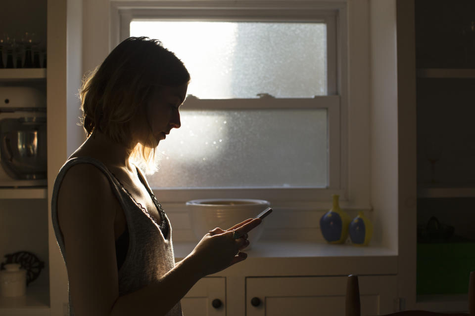 Silhouette of a person using a smartphone in a kitchen with soft light through a window