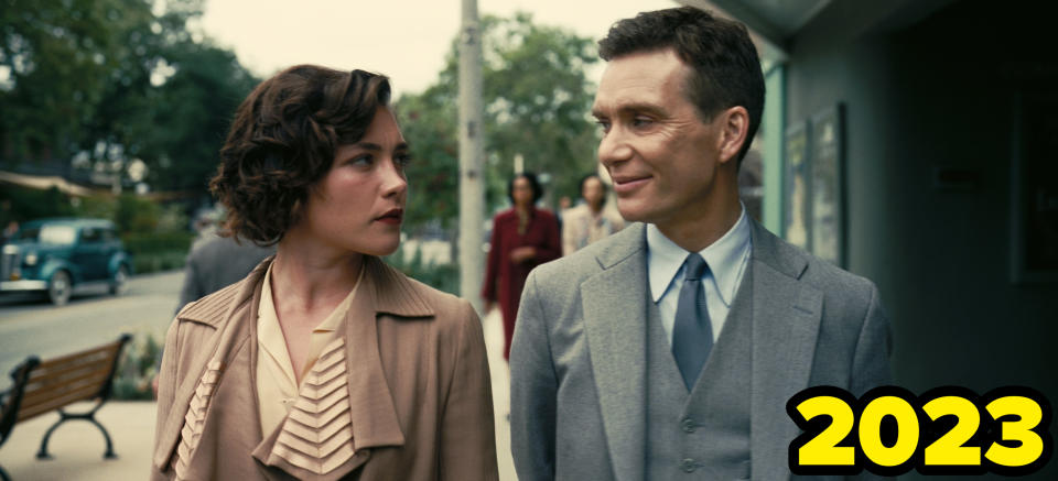 Florence Pugh and Cillian Murphy wear vintage attire as they walk on a street, exchanging a glance, in a scene from Oppenheimer