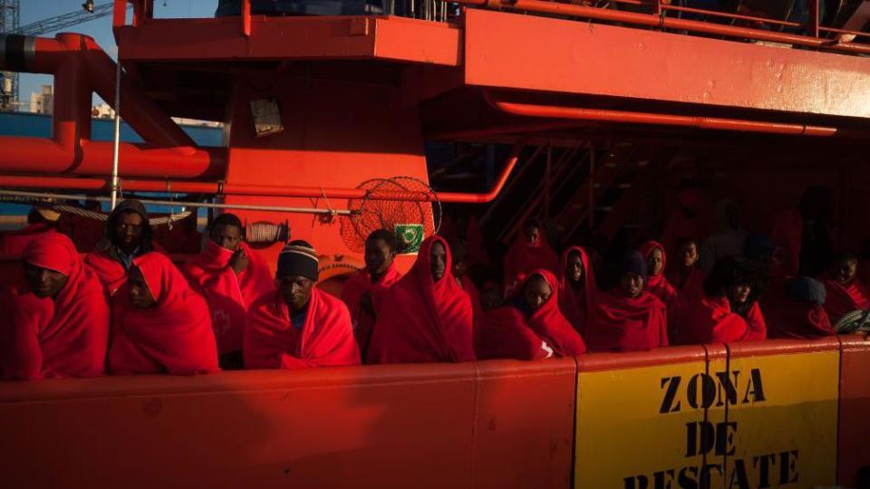 Migrants and refugees wearing blankets to stay warm are standing on a boat, operated by Spain's Maritime Rescue Service