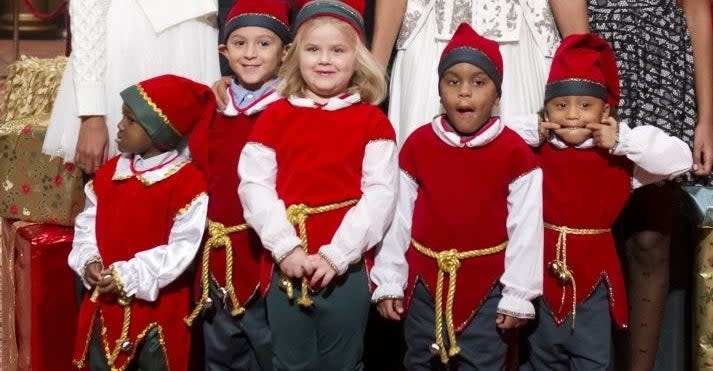 A family posing with children dressed as elves in front of a Christmas tree. Two adults in formal attire, three kids, and a plush Scooby-Doo toy