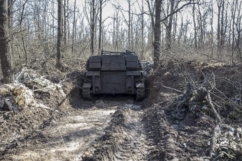 An armored fighting vehicle plows through a cluster of dead trees