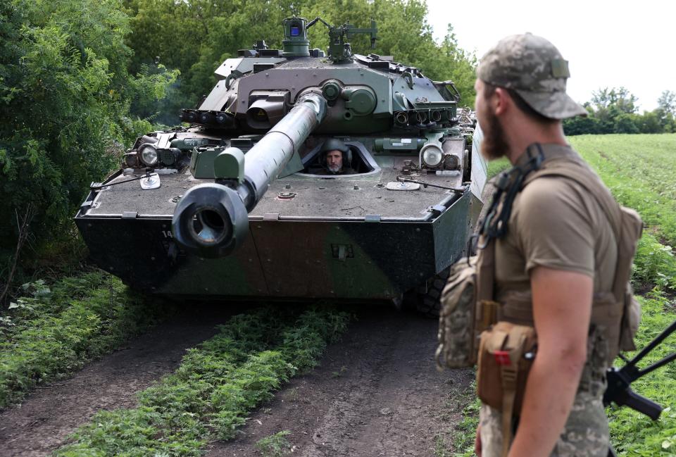 A man stands near an armored fighting vehicle as another man peers out from inside