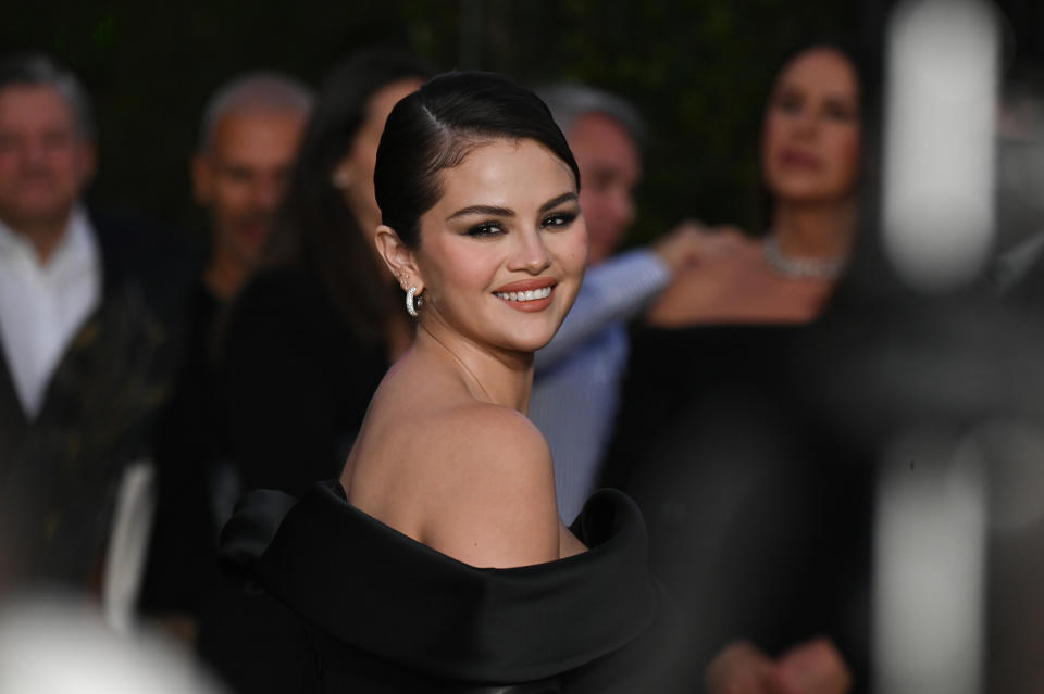 Person in elegant, off-the-shoulder dress smiling at a formal event. People in background