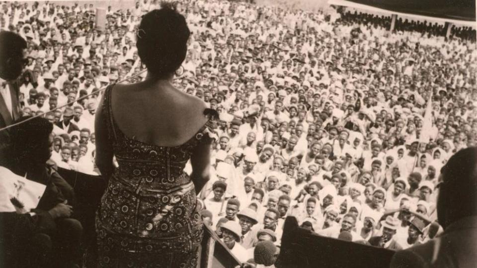 Wearing a patterened dress, Andrée gives a speech to a large crowd of men and women at a rally in the Democratic Republic of Congo