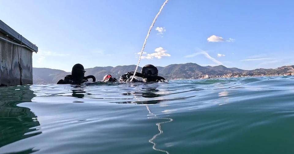 Special operations divers in the water, the mountains of Italy behind them.