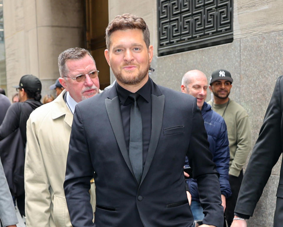 A man in a stylish suit walks outside, surrounded by people in casual attire