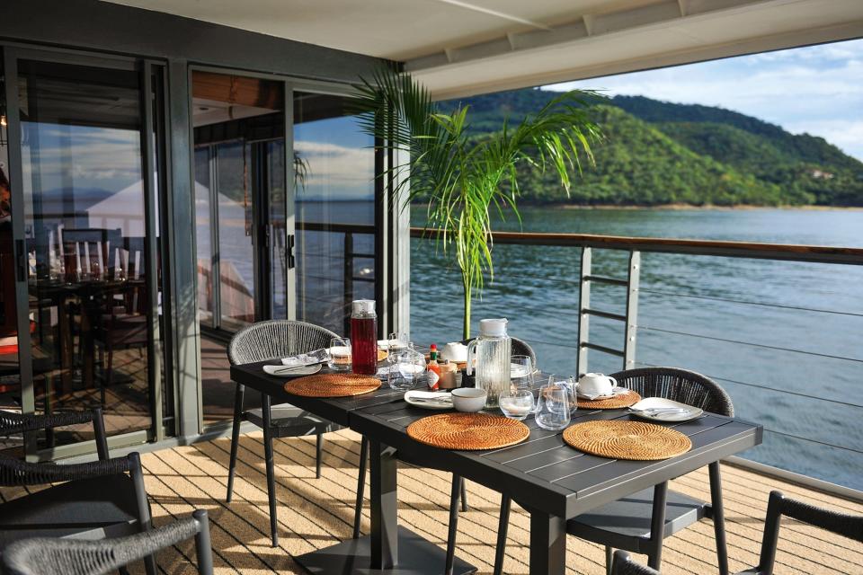 The wooden deck terrace aboard a cruiser with a palm plant and set dining table.