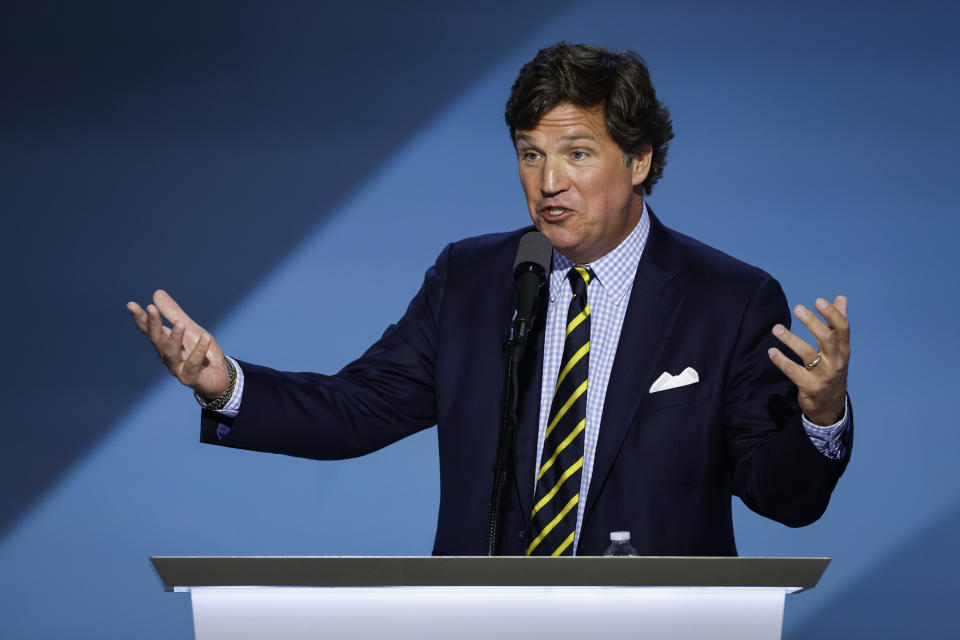 Person in suit with striped tie speaks animatedly at a podium on a stage