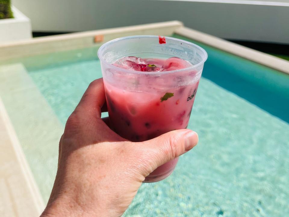 hand holding up a cocoberry mojito in front of an infinity pool