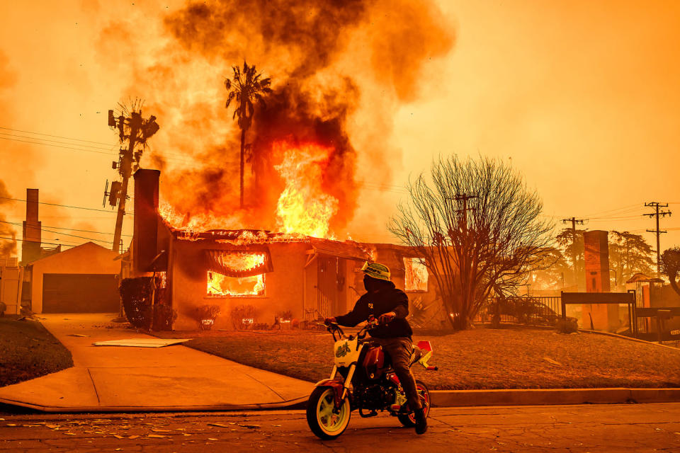 A motorcyclist stops to look at a burning home during the Eaton fire (Josh Edelson / AFP via Getty Images)