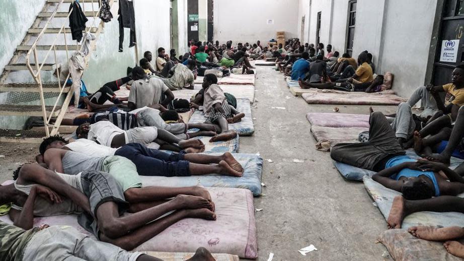 Dozens of men sleep on mattresses on the ground in a detention centre