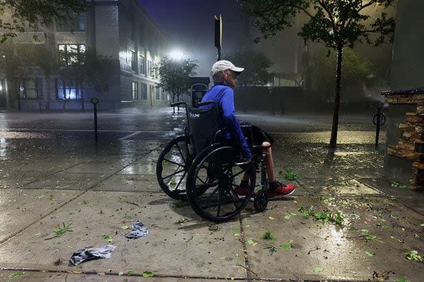 TAMPA, FLORIDA - OCTOBER 09: A woman in a wheelchair makes her way along a downtown sidewalk as Hurricane Milton makes landfall on October 09, 2024, in Tampa, Florida. Milton, coming on the heels of the destructive Helene, hit as a category 3 storm with winds of over 100 mph, though avoiding the projected direct hit on Tampa. Instead, the storm, which earlier had reportedly spawned tornadoes, landed about 70 miles south of Tampa near Siesta Key, a strip of white-sand beaches that's home to 5,500 people, according to published reports.  (Photo by Spencer Platt/Getty Images)