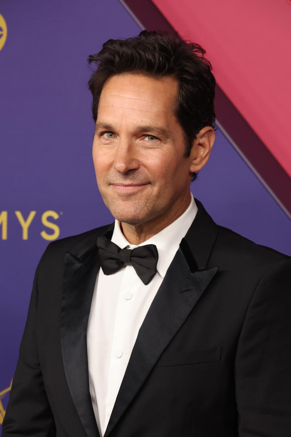 Person in a tuxedo on a red carpet, smiling at the camera