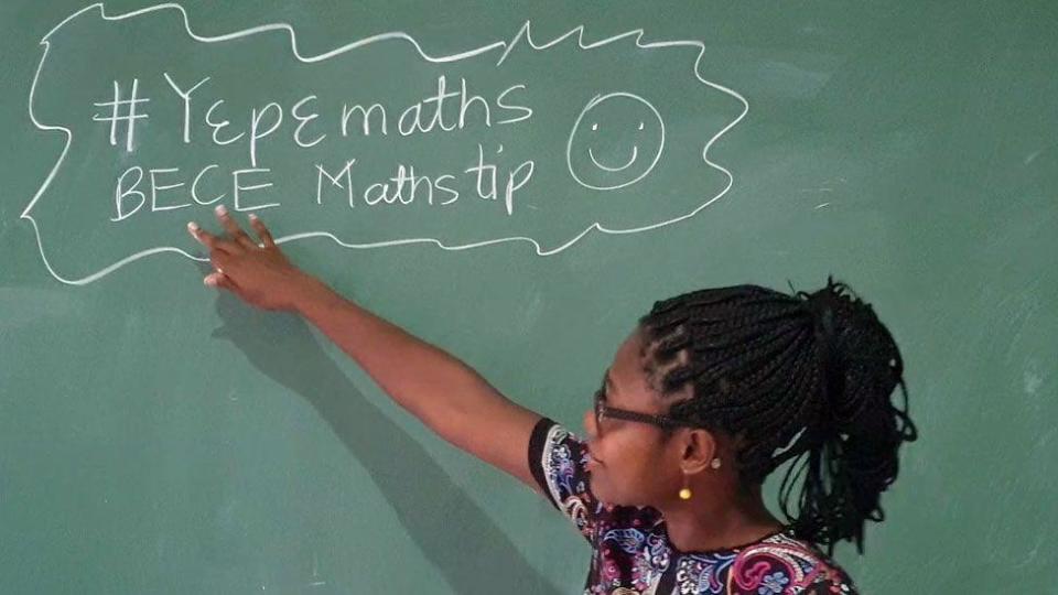 Dr Angela Tabiri look towards and pointing at a blackboard with some maths tips written in chalk during a FemAfricMaths YouTube lesson for junior high school students