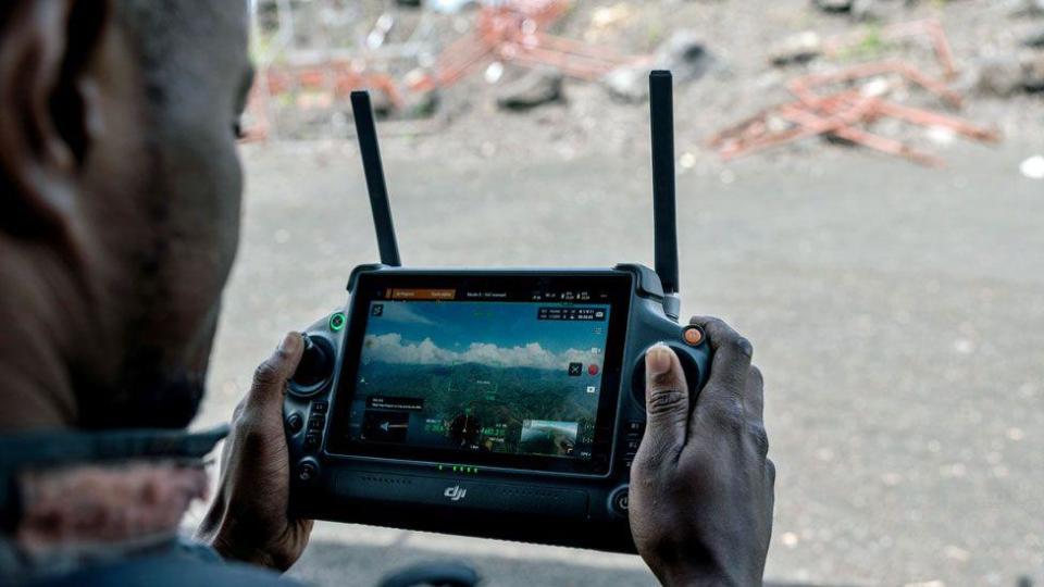 The hand of a Congolese soldier holds the controls for a drone. It has two antennae and its screen shows a view of hills in eastern DR Congo