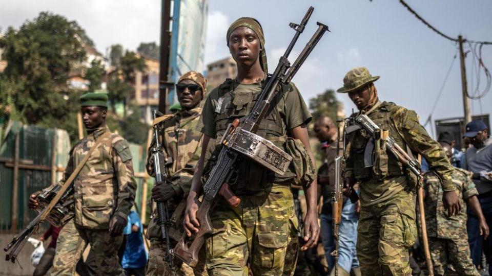 A group of M23 fighters, dressed in military fatigues, carry heavy weaponry