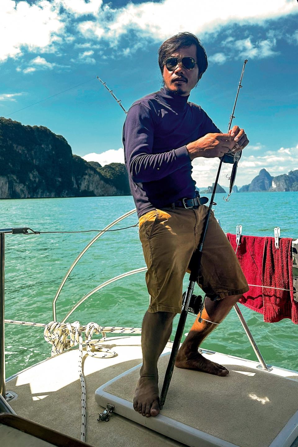 A Thai captain at the rear of a boat, prepping bait on a fishing rod.