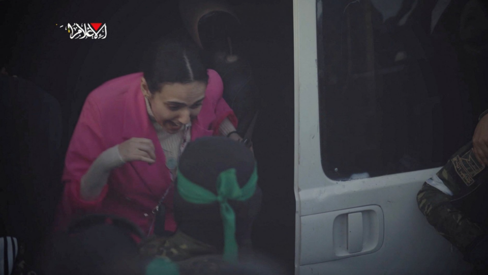 An excited Romi Gonen wearing a pink shawl steps out of a white Hamas van 