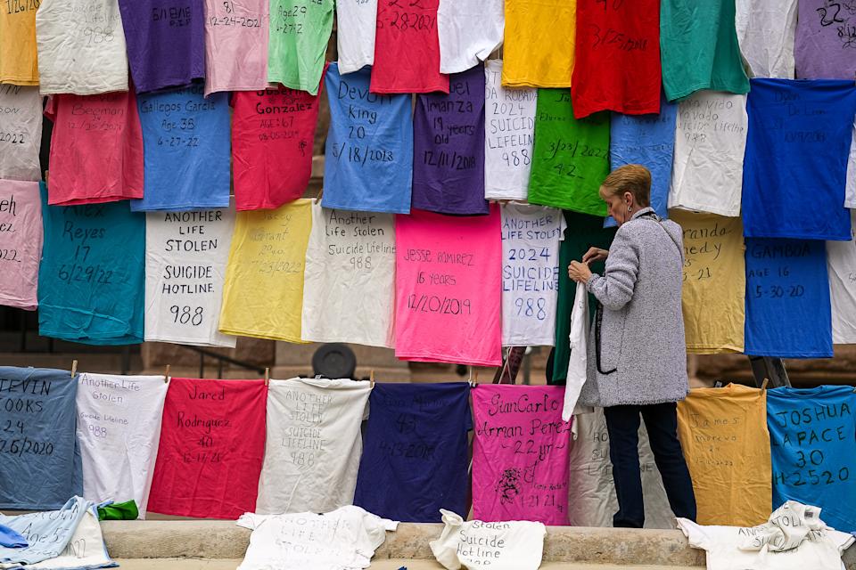 Judy Ward hangs shirts, each representing a Texas gun violence death, on a display Thursday ahead of the Texas Gun Sense Advocacy Day March.