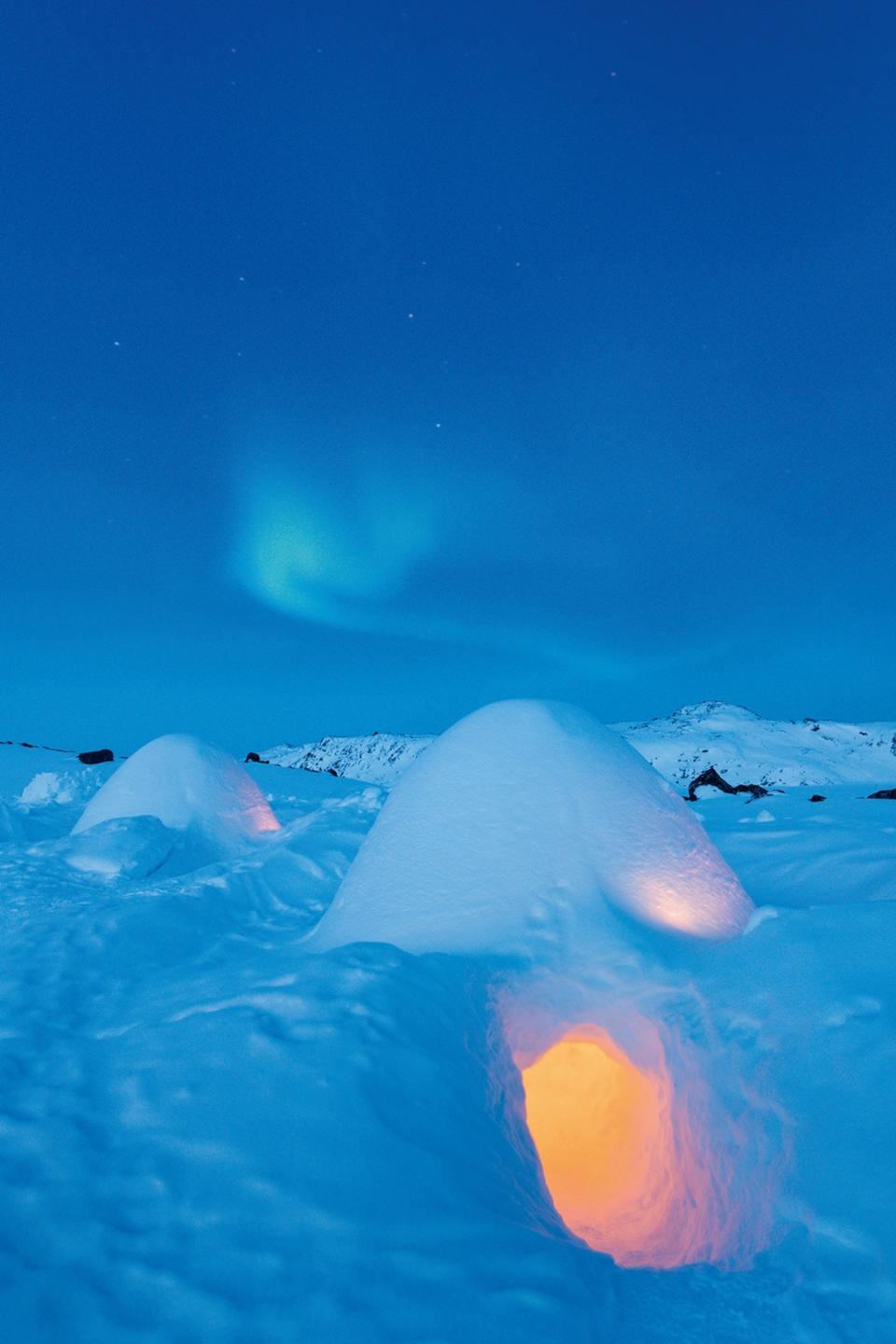 A snowed in Igloo lodge at night, one ice house lit with light from within.