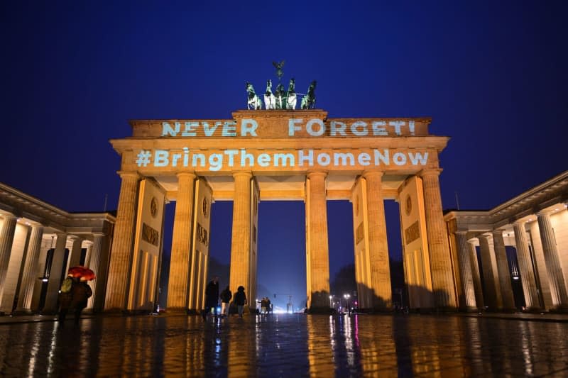 The words "Never forget" and "#BringThemHomeNow" are projected onto the orange-lit Brandenburg Gate during a memorial service to mark the funeral of the Bibas family members in Israel. Sebastian Christoph Gollnow/dpa