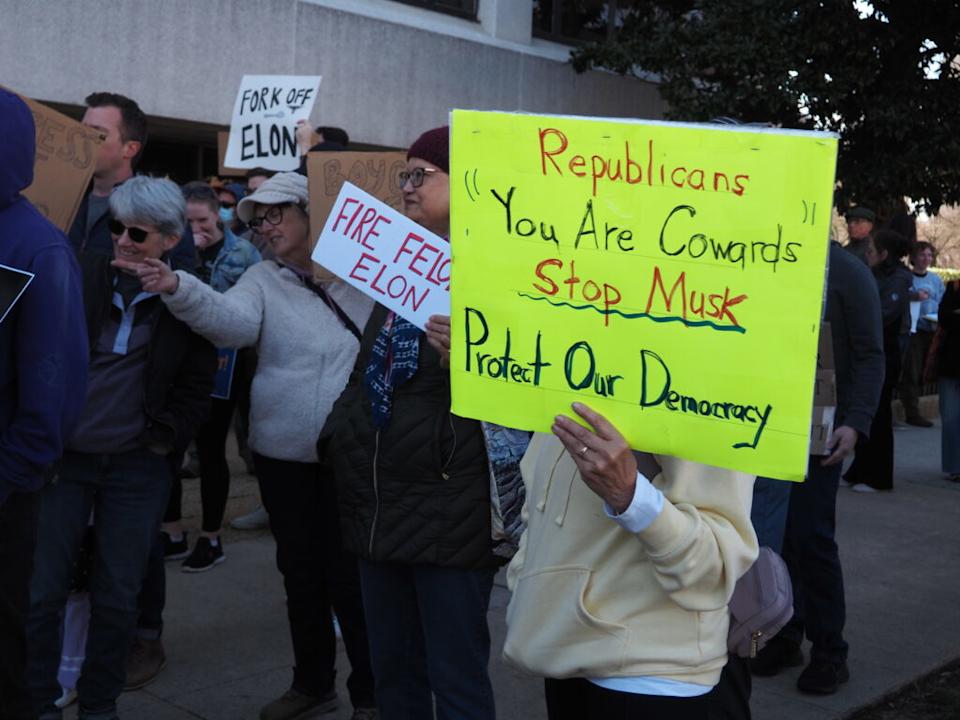 Protesters hold signs reading “Fire Elon Musk” and “Republicans You Are Cowards.”