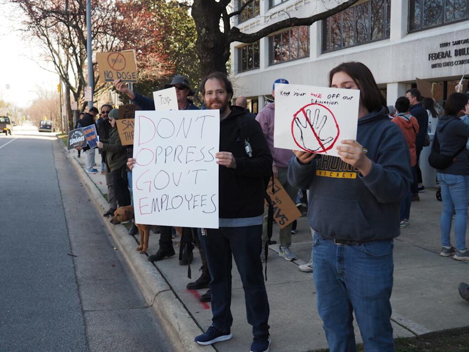 Protesters hold signs reading “Don’t Oppress Our Gov’t Employees” and “Keep Your Hands Off Our Education.”