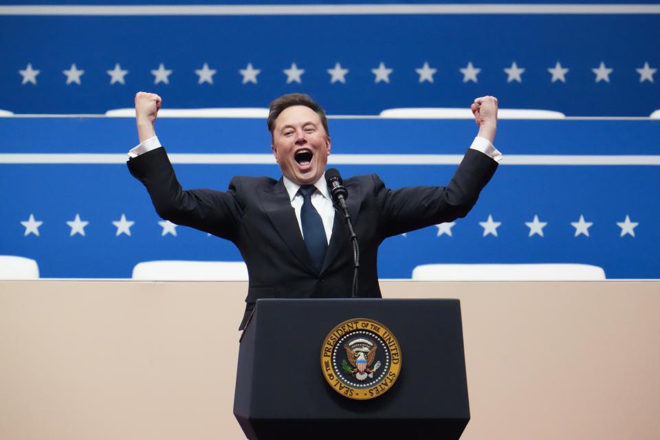 Elon Musk raising his arms and cheering from a podium.