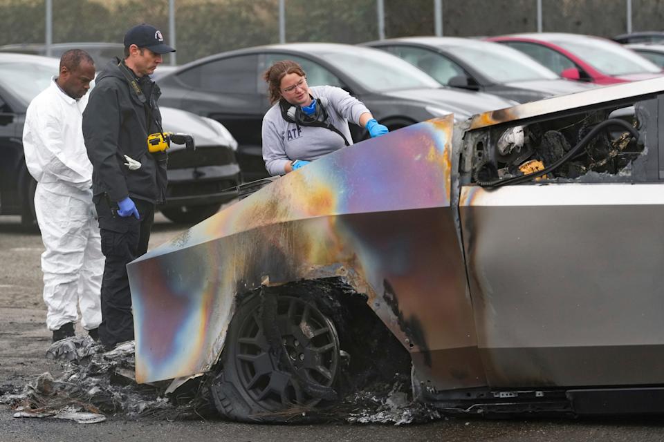 Three investigators looking at a burned Tesla Cybertruck at a Tesla lot.