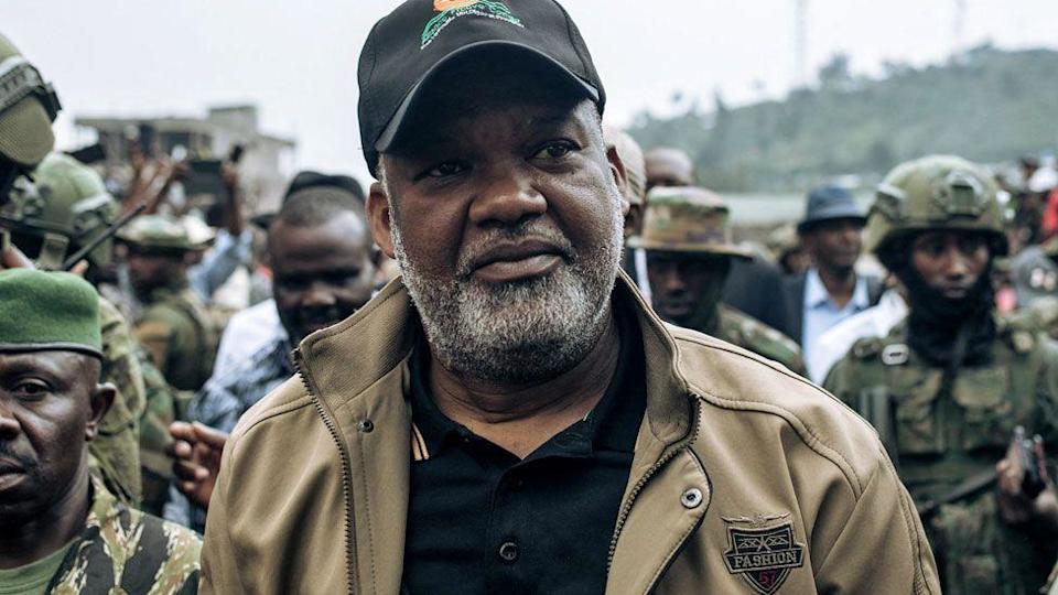 Congo River Alliance Corneille Nangaa, wearing black cap, black T-shirt and brown jackets, arrives at the Stade de l'Unite in Goma on February 6, 2025. He is surrounded by M23 fighters.