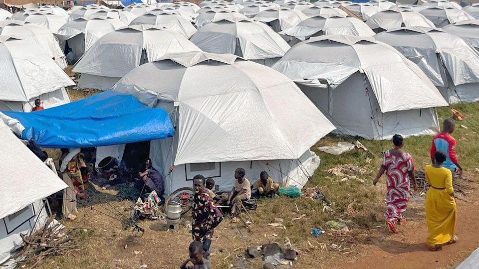 A sea of white tents seen at Rugombo football stadium with people seen outside some of them.