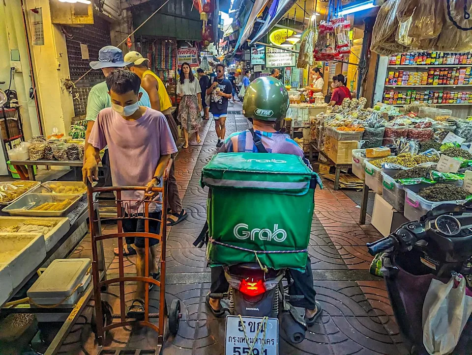 A Grab scooter driving down Sampeng Lane crowded with vendors and people. 