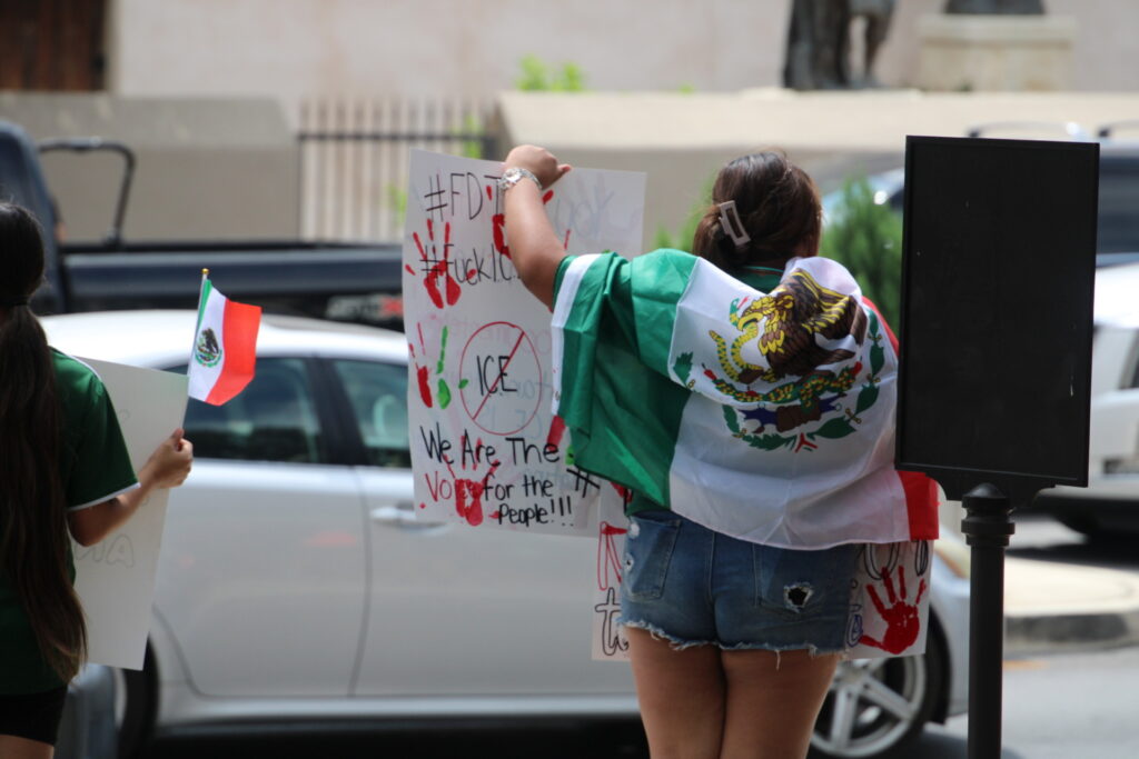 Protesters draped in Mexican flag carries sign with vulgar message at anti-ICE rally, photo by Randy Clark (Randy Clark/Breitbart Texas)