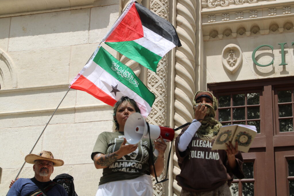 Protesters read anti-Israel, anti-ICE messages next to Palestinian flag at anti-ICE protest photo by Randy Clark (Randy Clark/Breitbart Texas)