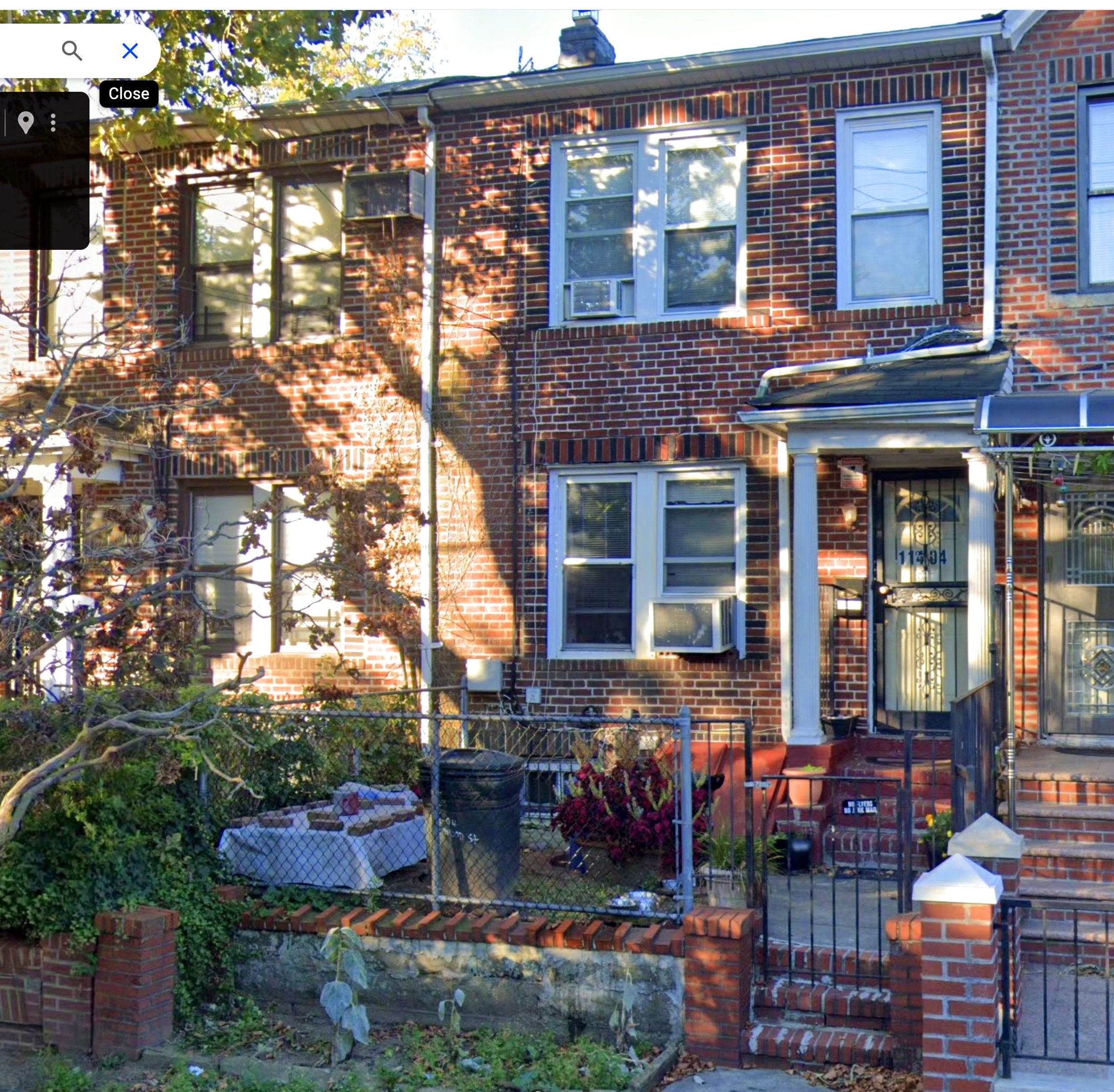 Brick townhouse exterior with front garden, featuring a fence and decorative plants in a residential neighborhood.