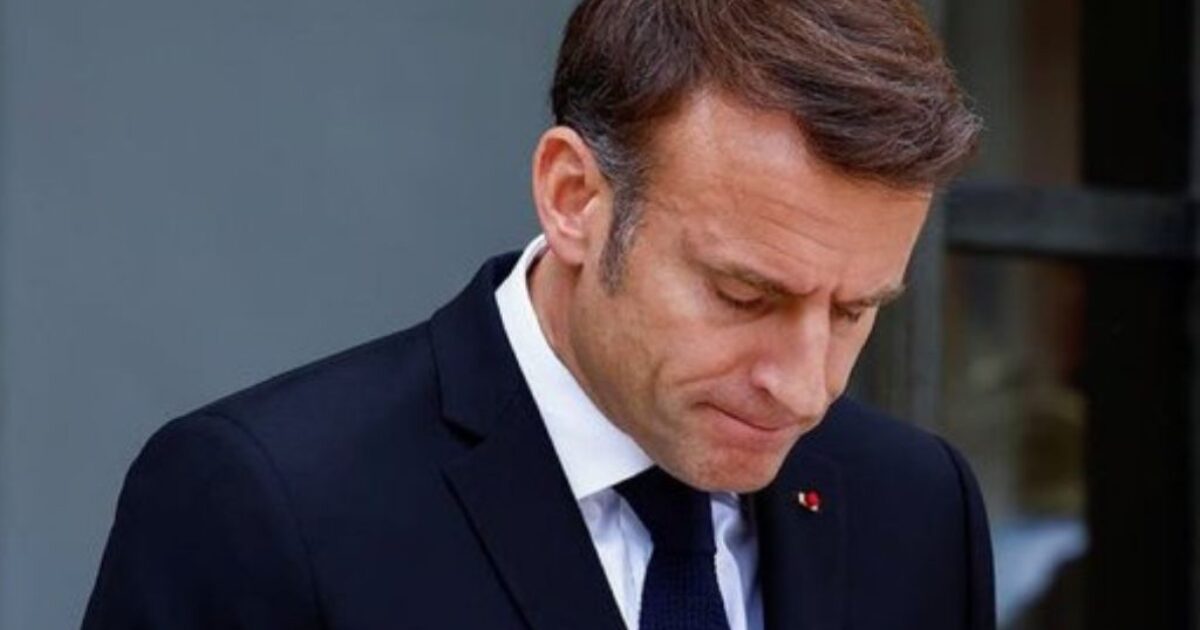 French President Emmanuel Macron looking down, dressed in a formal suit, conveying a serious demeanor during a public appearance.