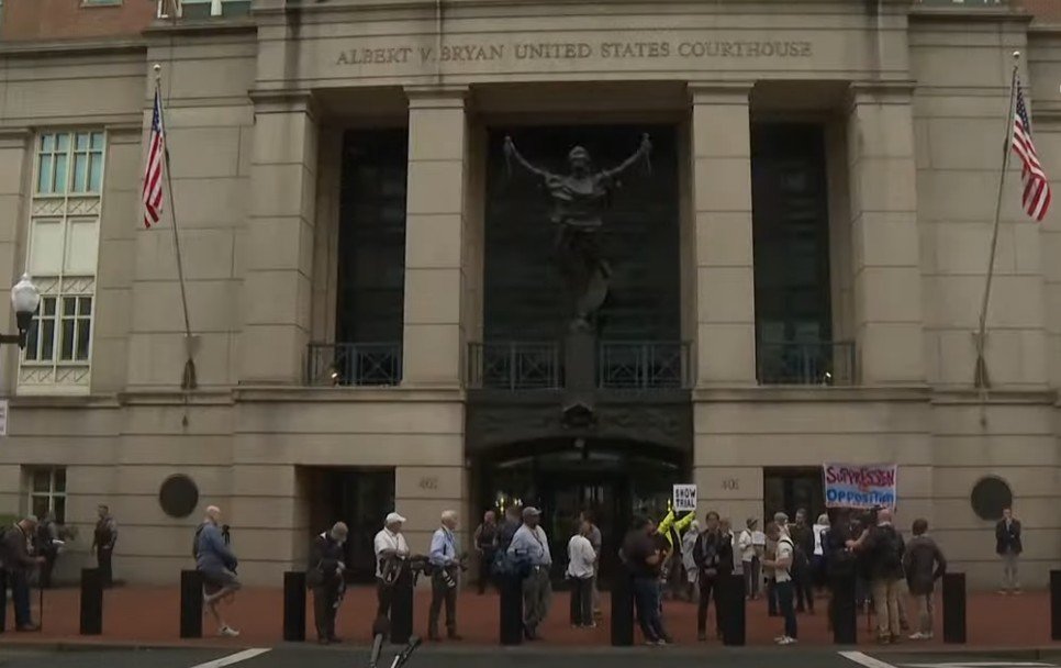 Crowd gathered outside the Albert V. Bryan United States Courthouse, with flags and signs visible, during a public demonstration.