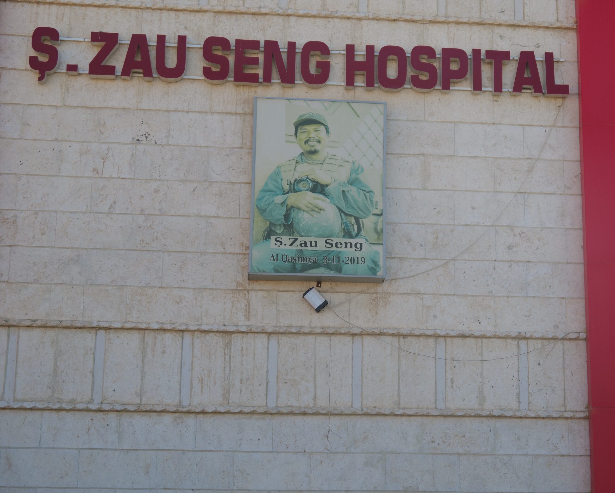 Signage for S. Zau Seng Hospital featuring a portrait of S. Zau Seng, located in Al Qasimya, with the date 3-11-2019 displayed.