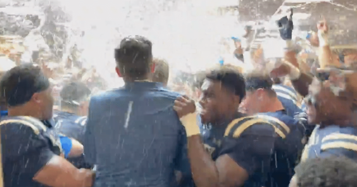 Celebrating football team members joyfully spraying each other with confetti and water in a locker room after a victory.