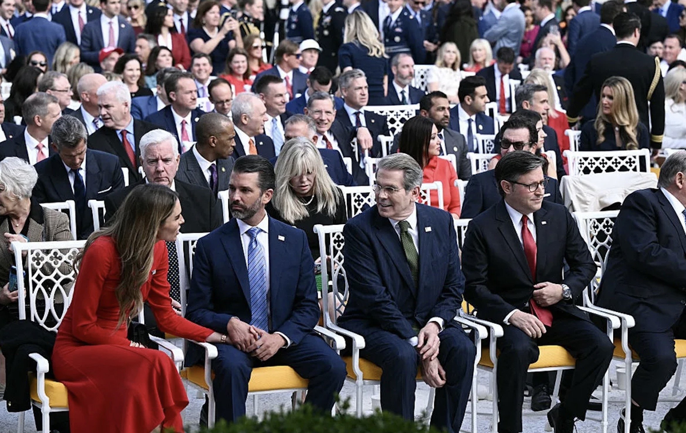 A diverse group of attendees seated in a formal outdoor setting, engaging in conversation during a significant event.