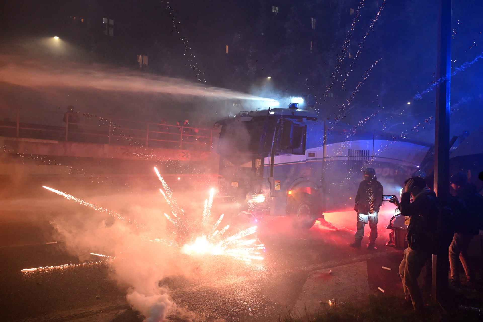Fireworks explode next to a police truck spraying water to demonstrators during a protest against the environmental, economic and social impact of the Milano-Cortina 2026 Winter Olympics Games, in Milan on February 7, 2026. (Photo by PIERO CRUCIATTI / AFP via Getty Images)