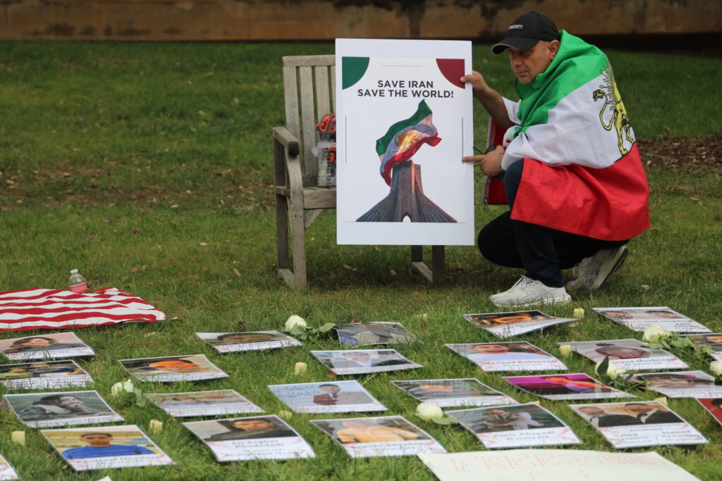 Man kneels with photos in memory of Iranians killed by their government. (Randy Clark/Breitbart Texas)