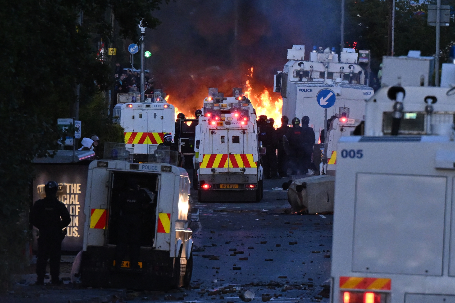 MALLUSK, NORTHERN IRELAND - JUNE 10: Fire burns near police vans as protests take place near the Chimney Corner Hotel, which allegedly may be a hotel housing migrants, following a night of anti-immigrant riots on June 10, 2026 in Mallusk, Glengormley, Northern Ireland. Overnight protests in Belfast turned violent in reaction to a knife attack that took place on Monday night, which left a male victim in his 40's with serious injuries. Homes and vehicles were torched following the Home Office's confirmation that the suspected knifeman is a 30-year-old asylum seeker from Sudan, who was in the UK on leave to remain. Far-right influencers have been accused of stoking the violence by calling for anti-immigrant demonstrations after a graphic video of the stabbing attack went viral on social media. (Photo by Charles McQuillan/Getty Images)