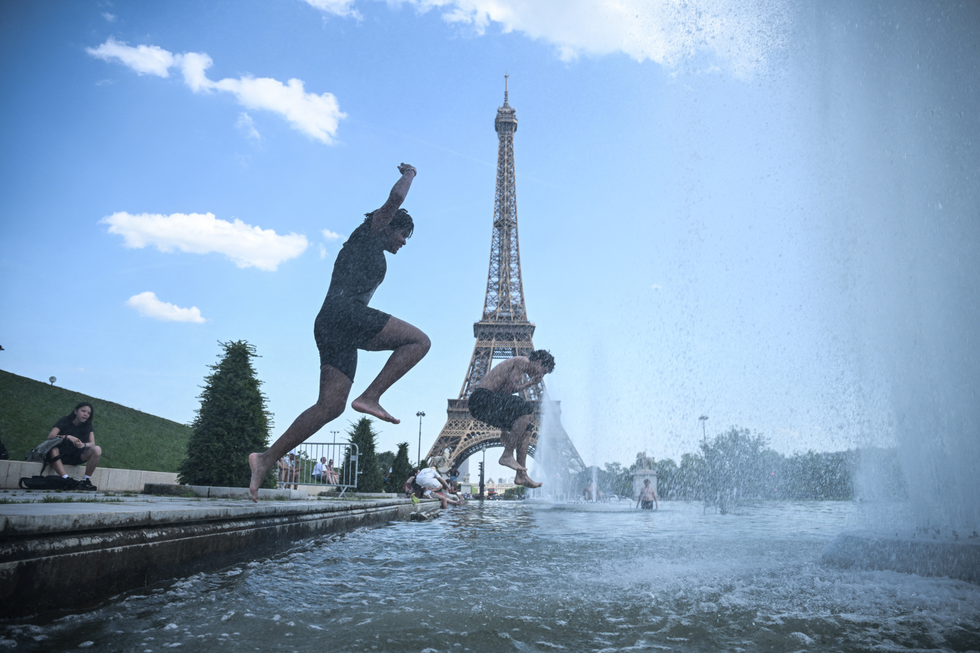 TOPSHOT - People jump in the Trocadero Fountain near the Eiffel Tower during a heatwave in Paris on June 22, 2026. The latest bout of exceptionally high temperatures to hit Europe has seen outdoor events cancelled, transport disrupted, schools shut and office workers told to work from home, as the authorities issued health alerts to protect the elderly and vulnerable. In France, the epicentre of the weather anomaly, 54 of the country's 96 mainland departments were on the highest heat alert, with temperatures forecast to climb up to 43C in the southwestern city of Bordeaux and 39C in the capital Paris, said national weather service Meteo-France. (Photo by JULIEN DE ROSA / AFP via Getty Images)